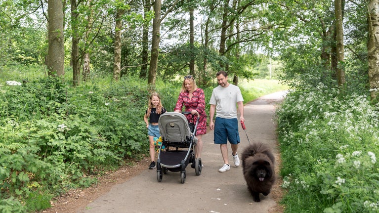Family walking along a path with a pushchair and dog.